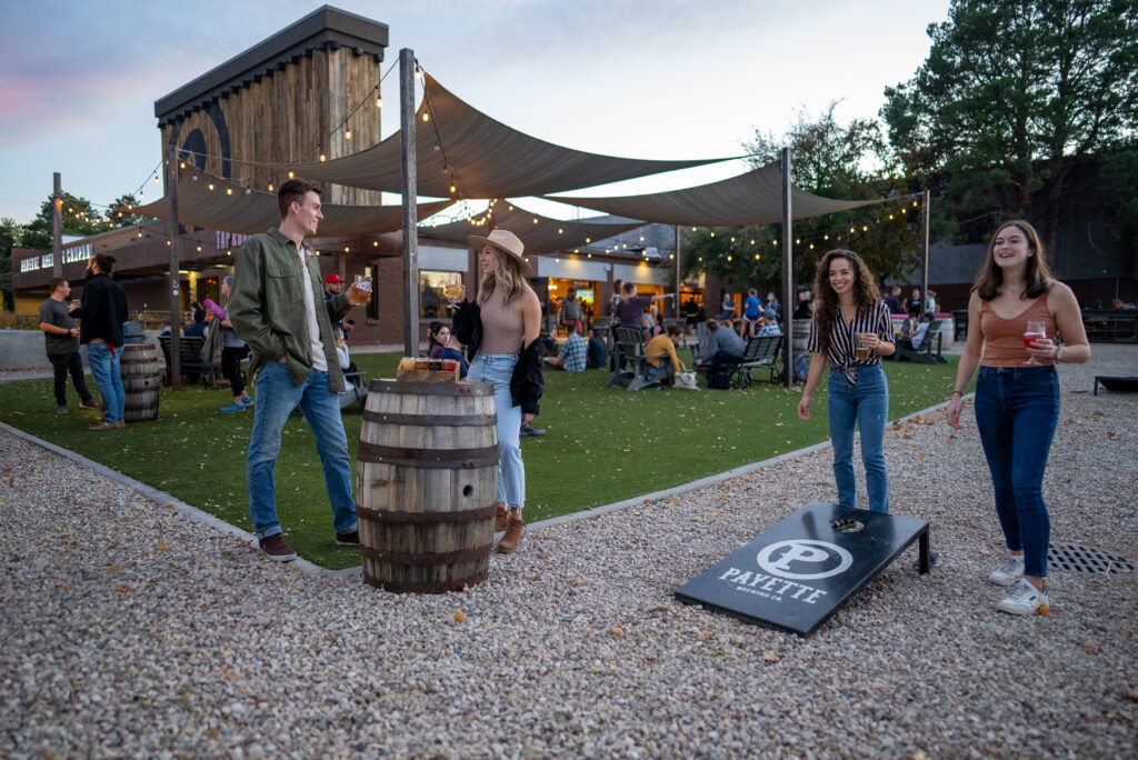 Friends playing cornhole at a Boise brewery patio at dusk